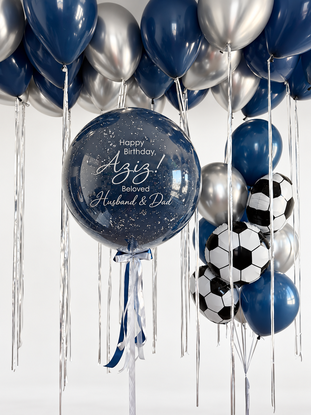 Personalized navy bubble with silver speckled details beside a bouquet of navy and silver latex balloons and three soccer ball foil balloons, beneath matching ceiling balloons.