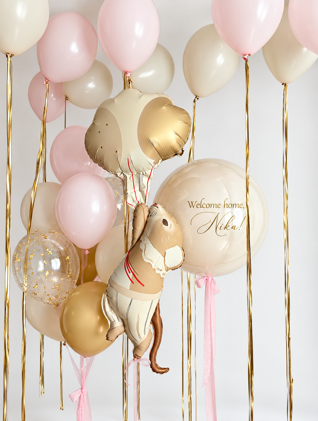 Mouse holding balloons foil figure beside a personalized cream bubble and a pink, cream, gold and confetti balloon bouquet, with matching ceiling balloons and gold ribbons.
