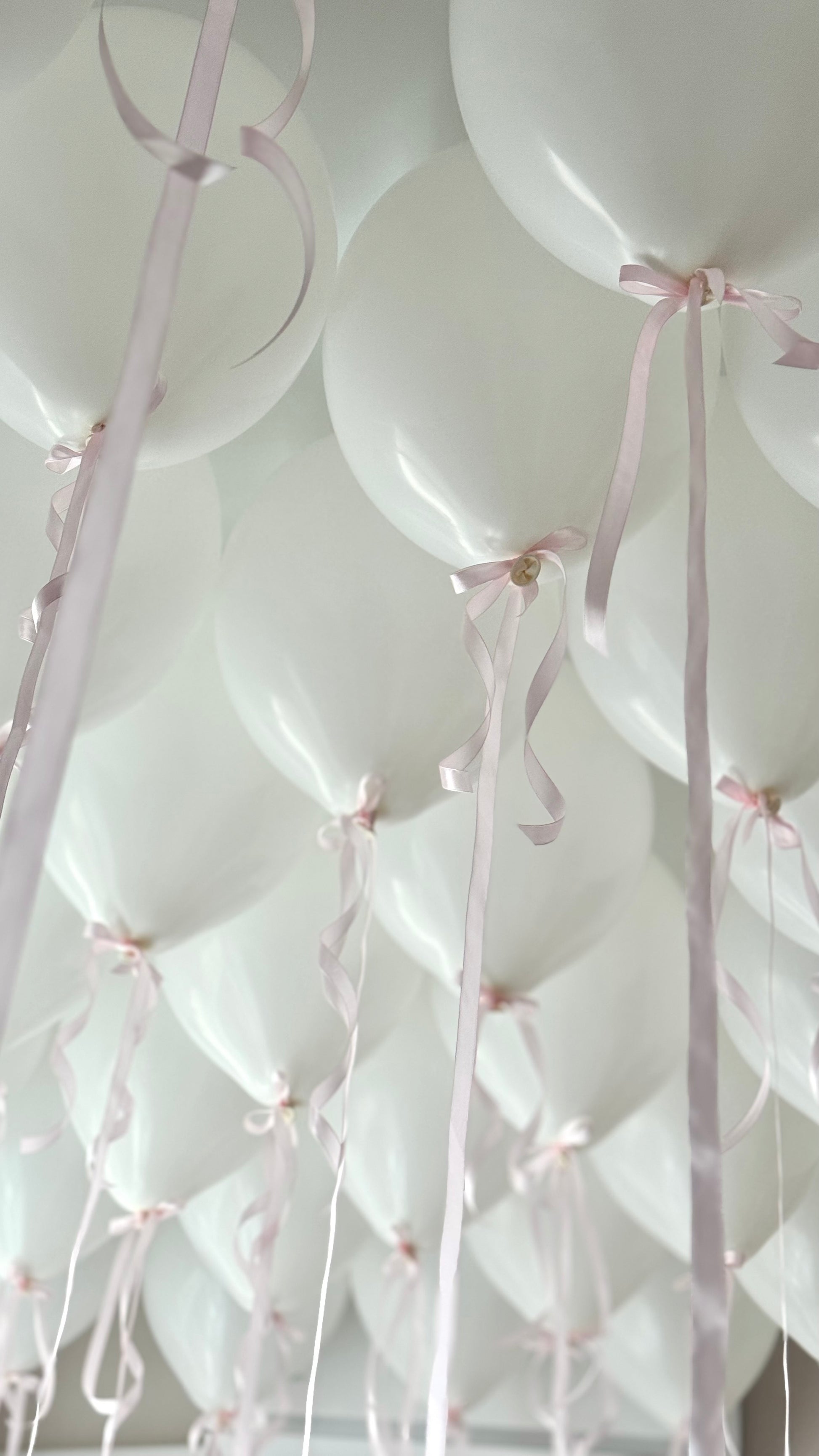 White helium ceiling balloons with pink ribbon bows in New York City
