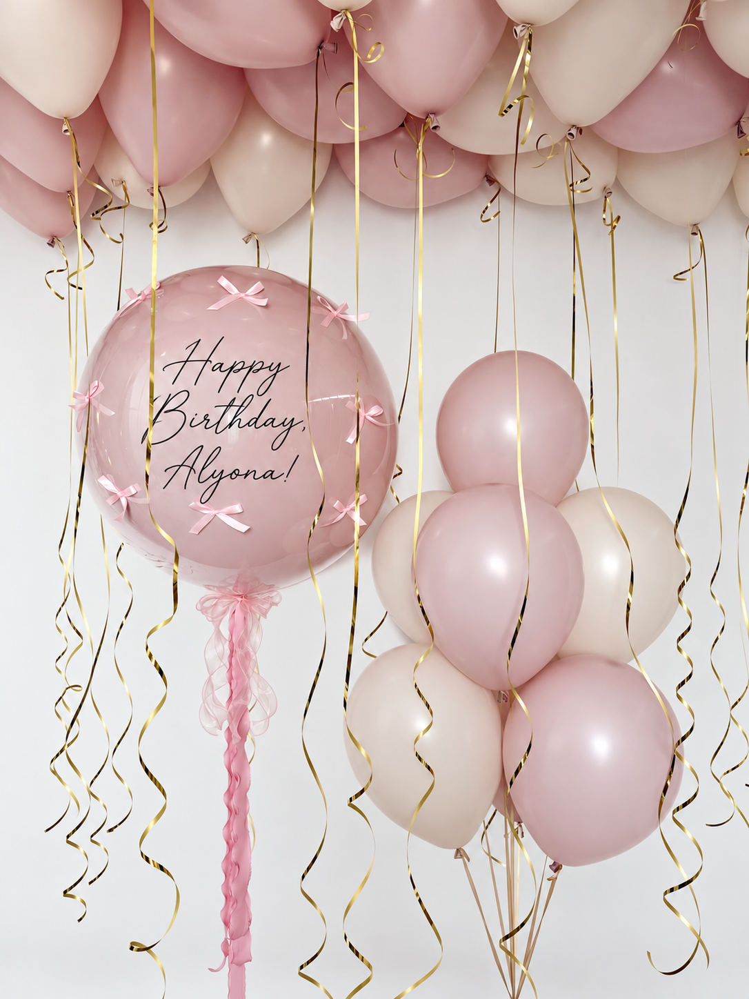 Personalized dusty pink bubble with small pink bows and flowing pink ribbons, a pink and cream latex balloon bunch, and matching ceiling balloons with gold ribbons.