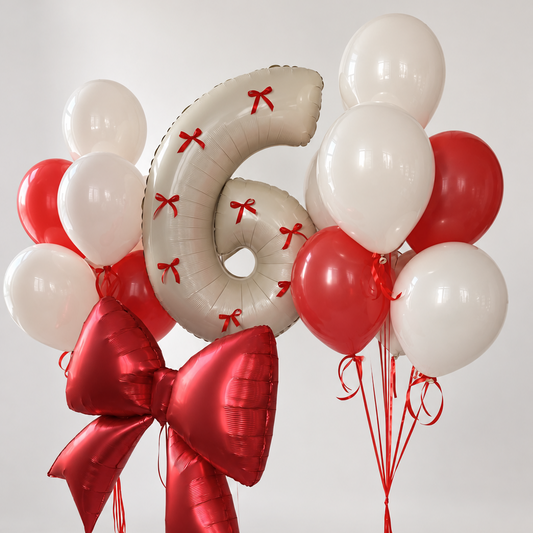 Cream number six balloon decorated with small red bows, a large red foil bow and two bunches of cream and red latex balloons.