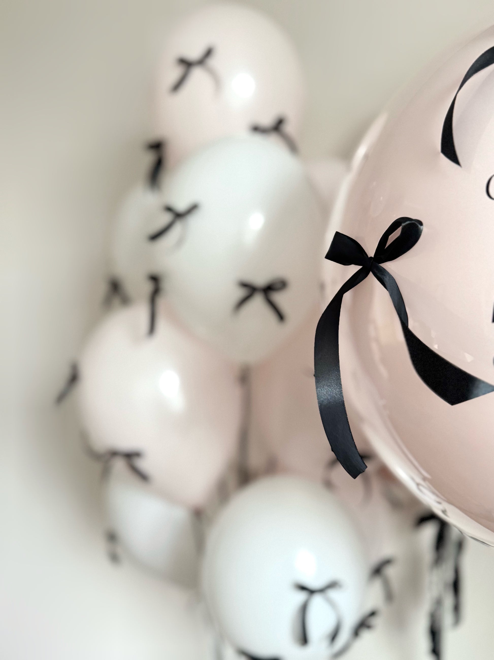 Close-up of blush and white birthday balloons with black bows for girls party decor in Brooklyn