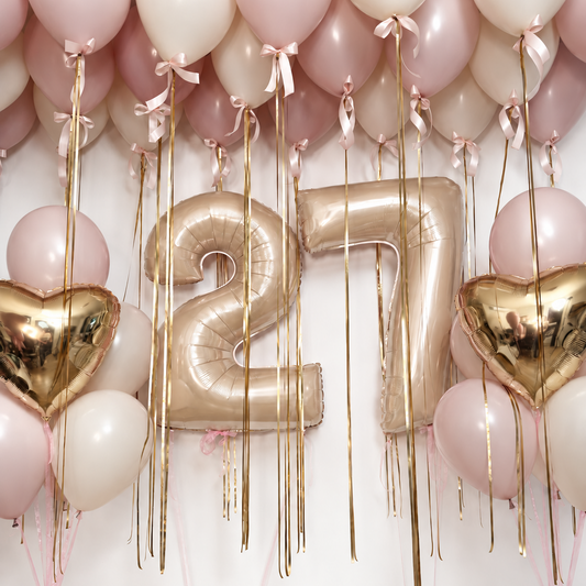 Golden blush birthday balloon set with gold number balloons, foil heart bouquets, and pink and ivory ceiling balloons finished with bows.