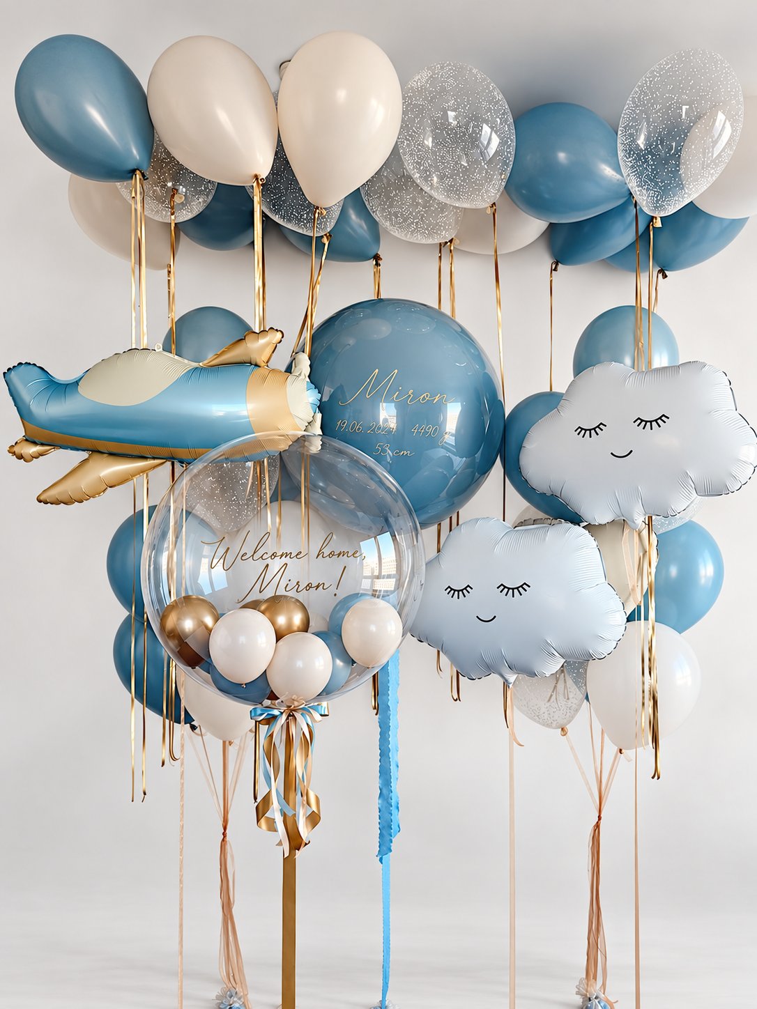 Blue and cream baby welcome balloons with two personalized bubbles, two smiling clouds, a blue and gold airplane, ceiling balloons and two coordinating bunches.