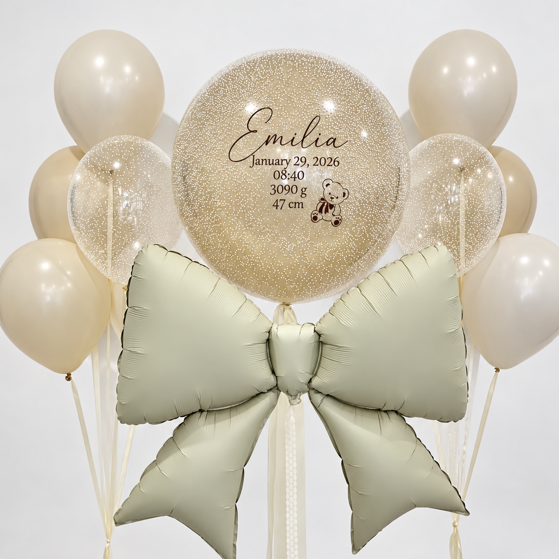 Personalized cream bubble with white speckled details above a large pale sage bow, framed by two bunches of cream and clear speckled balloons.