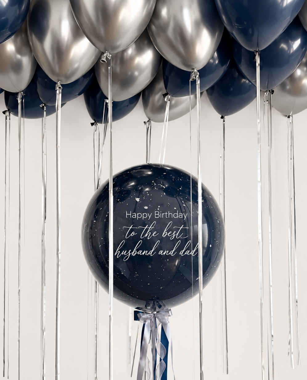 Personalized navy blue bubble balloon with white birthday lettering and navy and silver ribbons beneath navy blue and metallic silver ceiling balloons.