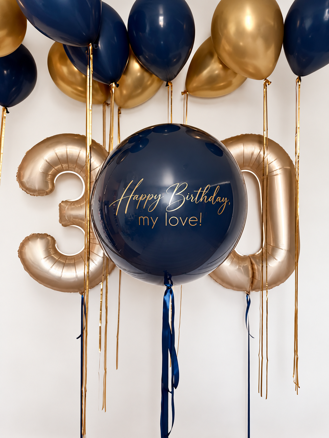 Personalized navy bubble balloon with gold birthday lettering, gold number 30 balloons, and navy and metallic gold ceiling balloons with gold ribbons.