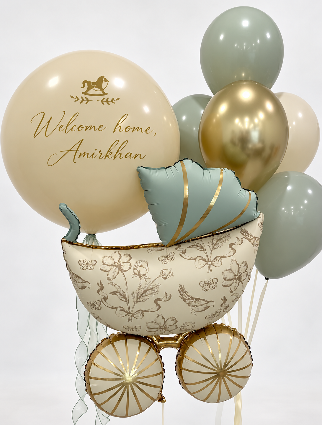 Large personalized cream balloon with gold lettering beside a sage and cream baby carriage foil balloon and a bunch of sage green, cream and metallic gold balloons.