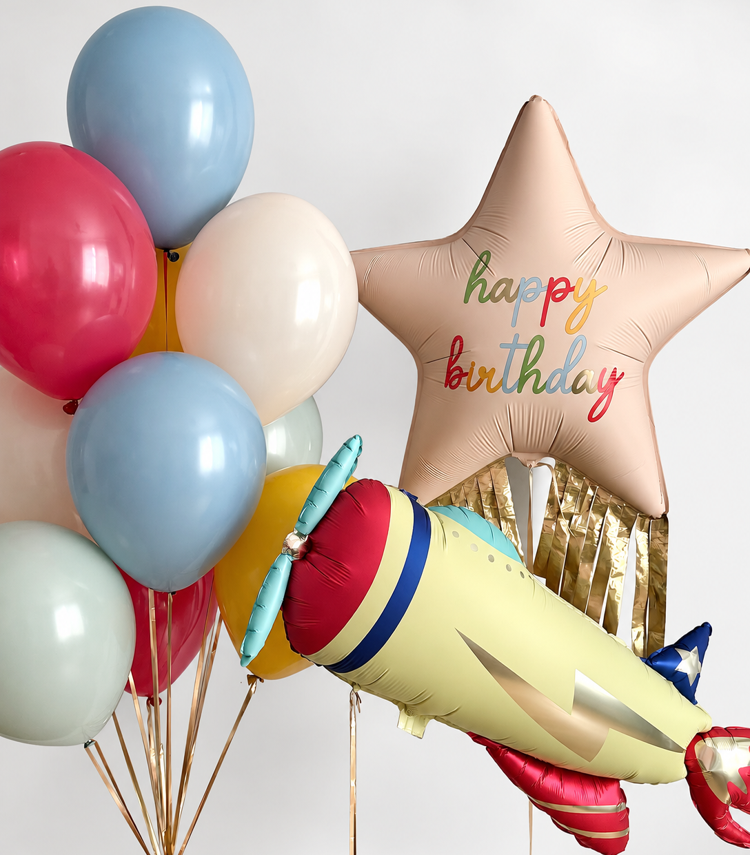 Colorful latex balloon bunch beside a cream birthday star with gold fringe and a vintage airplane foil balloon.