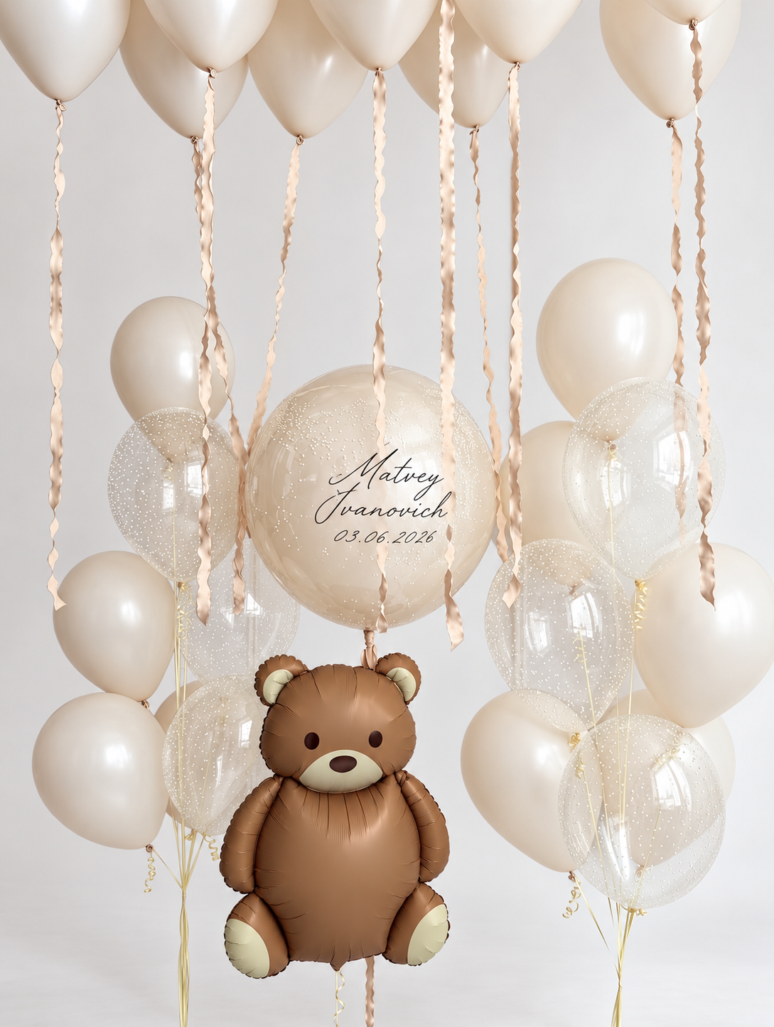 Brown teddy bear balloon below a personalized cream bubble, with two bunches of cream and clear speckled balloons and cream ceiling balloons with wavy ribbons.