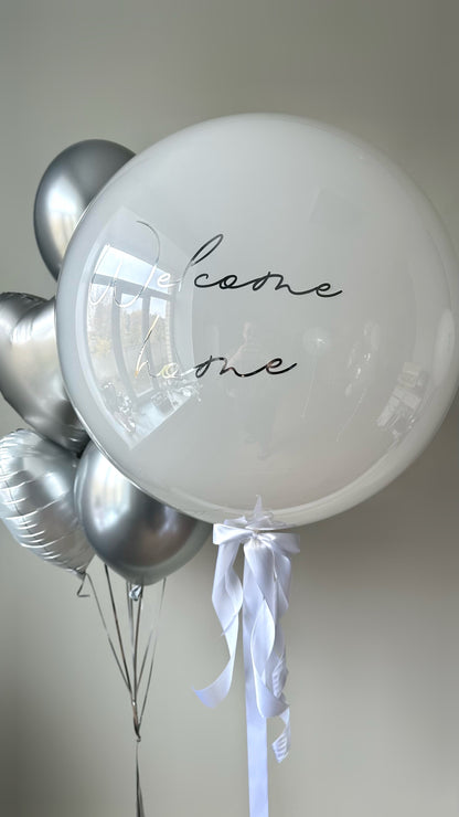 Close-up of warm welcome balloon set with white custom sign balloon and silver heart balloons in Brooklyn