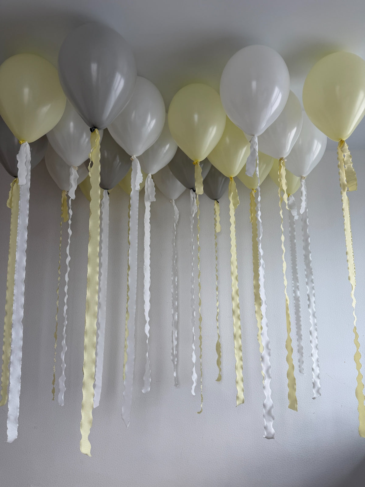 Yellow, gray and white helium ceiling balloons with long yellow and white wavy ribbons.